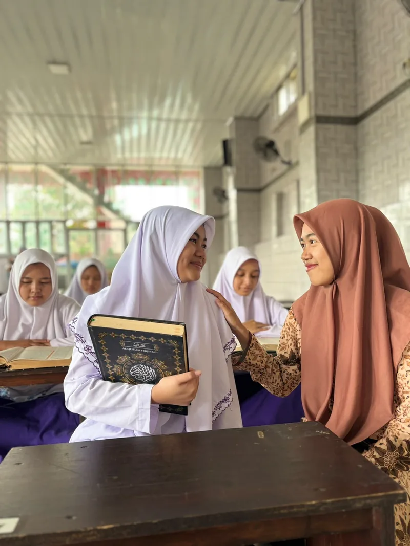Seorang pembimbing berbincang dengan santri yang memegang Al-Qur’an